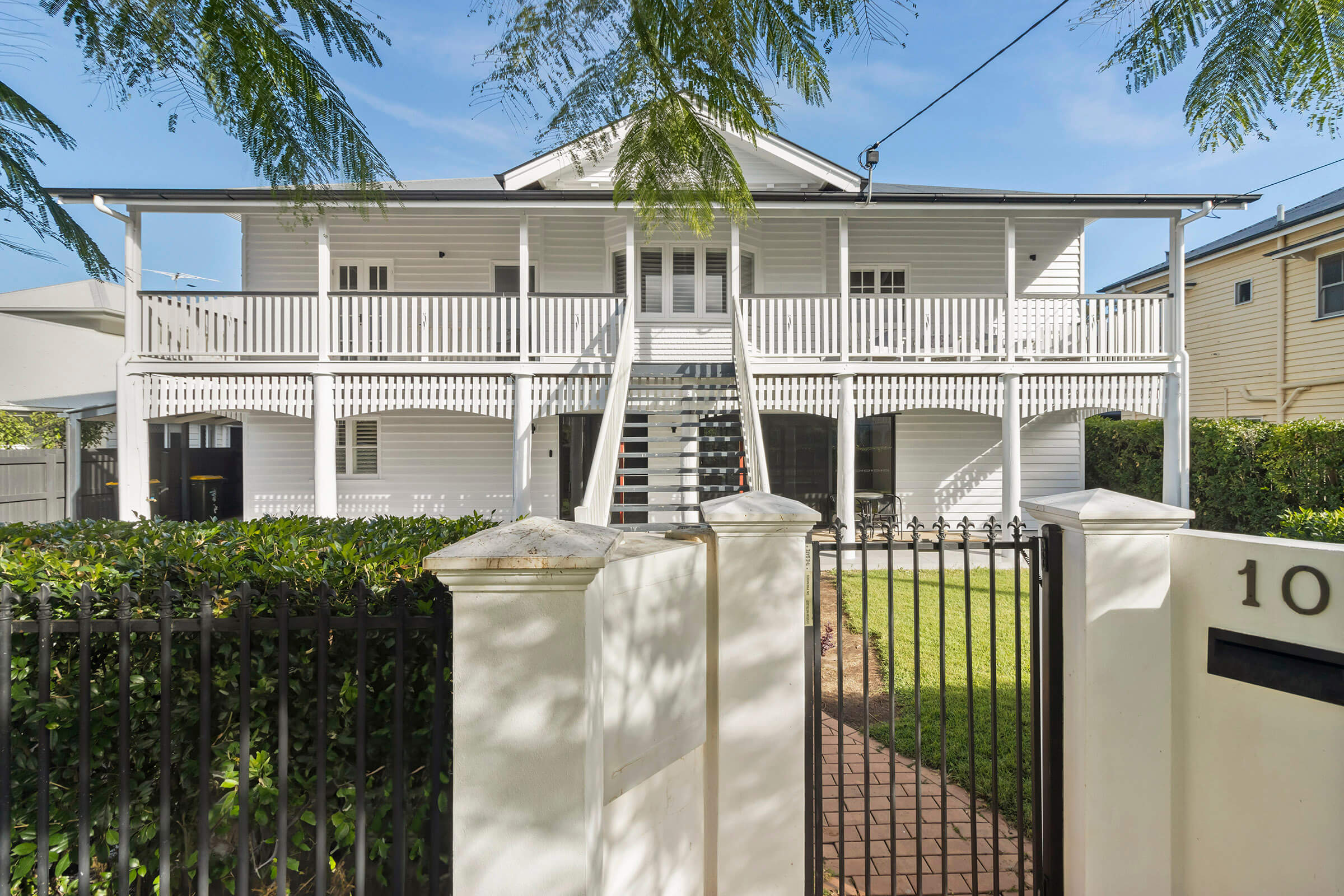 Classic white elevated home with front stairs, wraparound veranda, and fenced front yard.