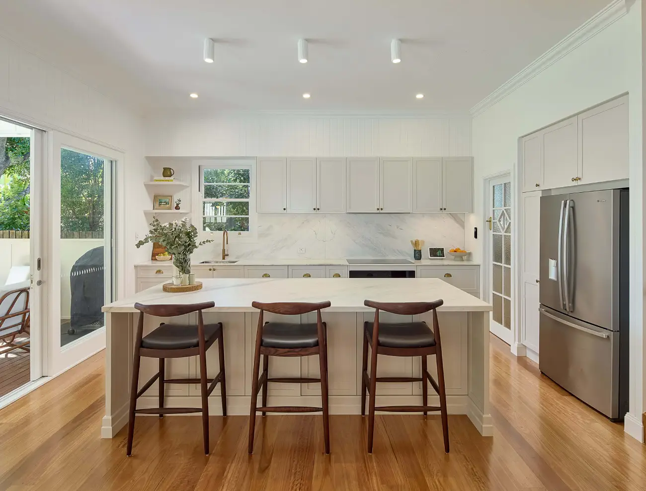 Bright modern kitchen with island bench, bar stools, and timber flooring.