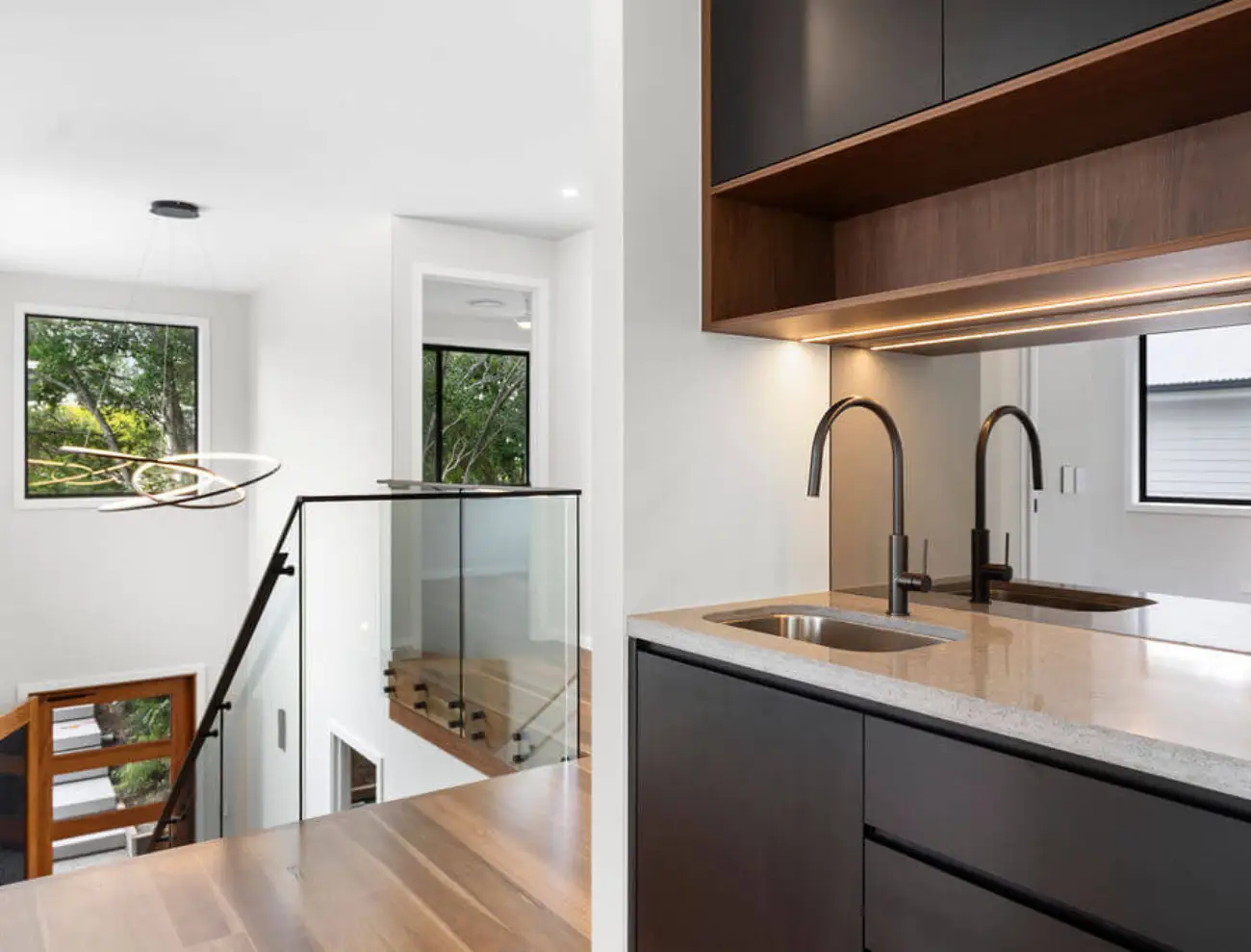 Modern upper-level kitchenette with black cabinetry, sink, and glass stair balustrade.