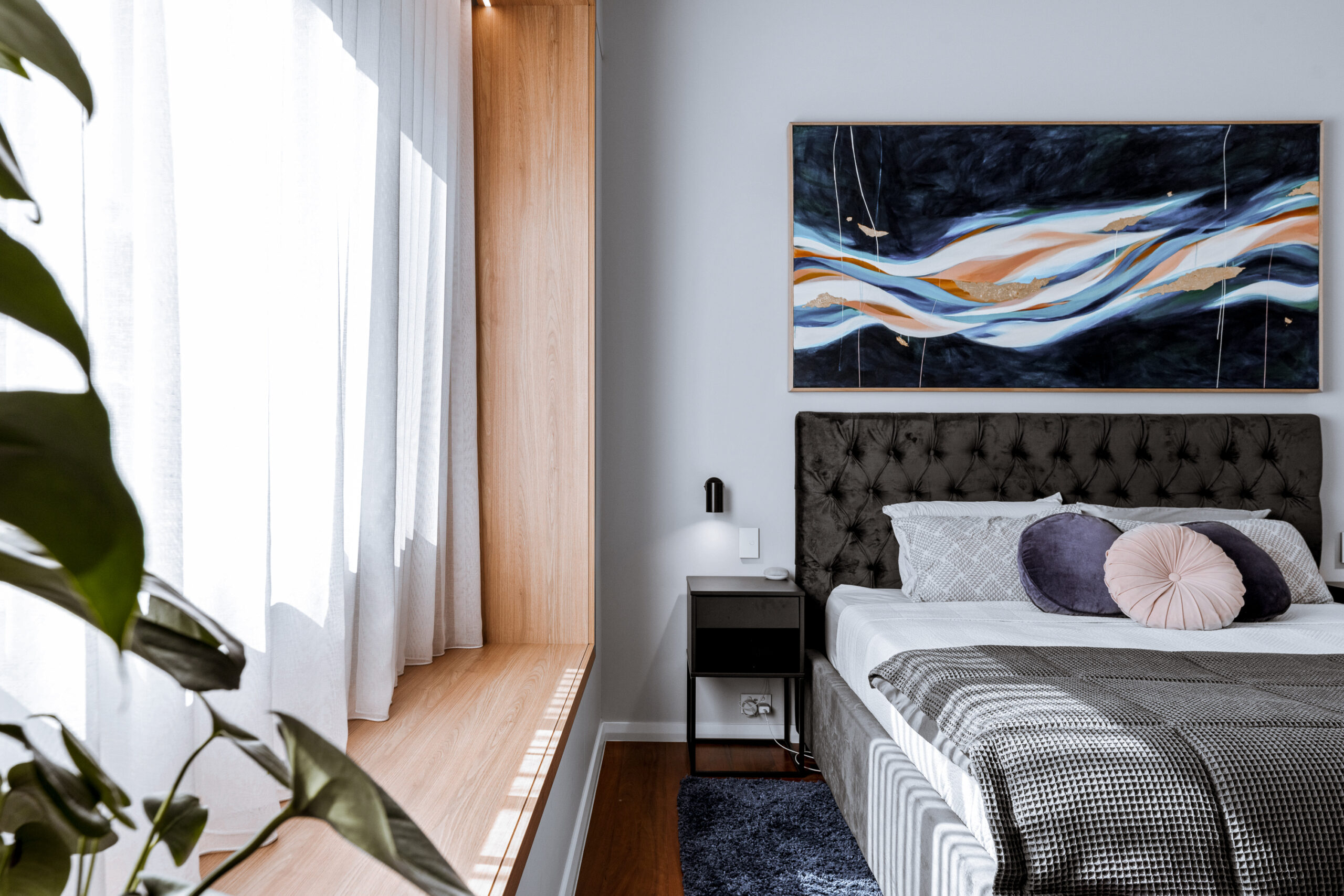 Cozy bedroom with a large painting, soft pillows, and a window bench.