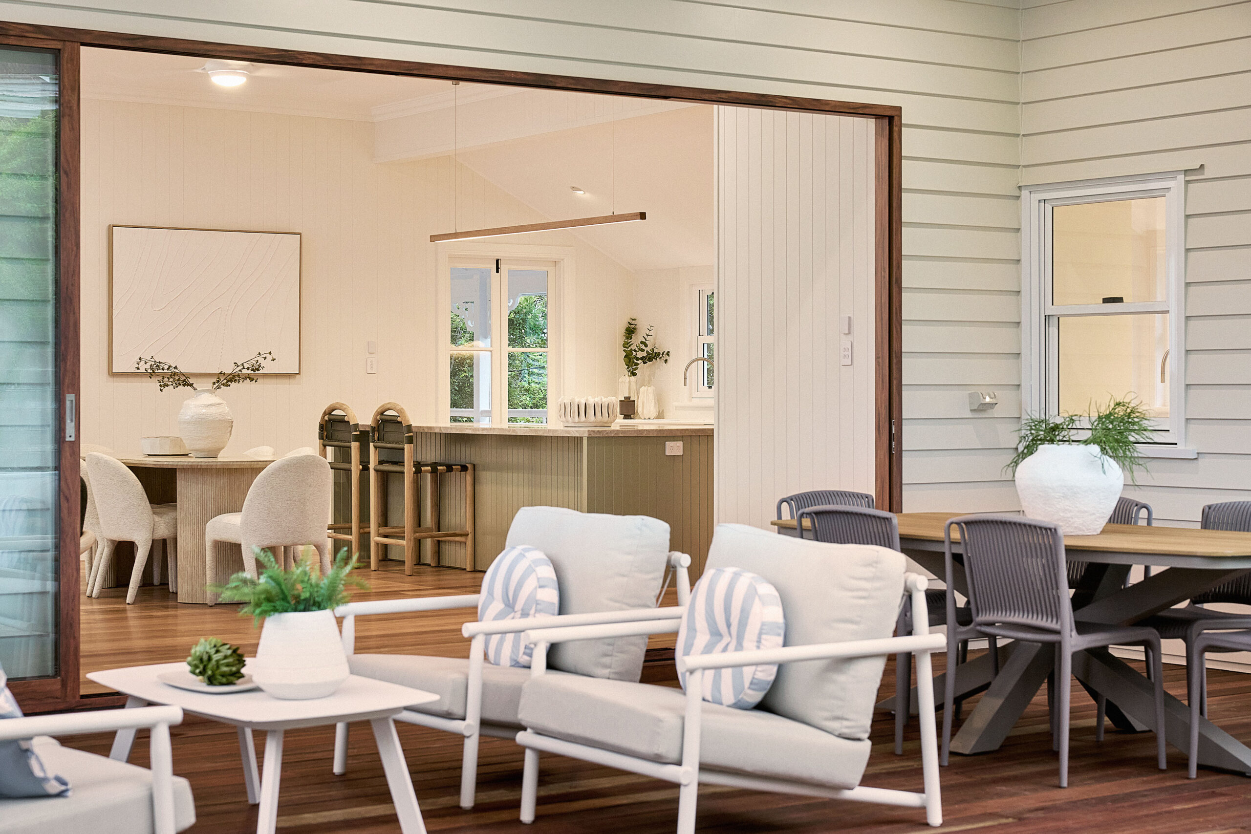 Outdoor patio with lounge seating, dining table, and open view into a modern kitchen